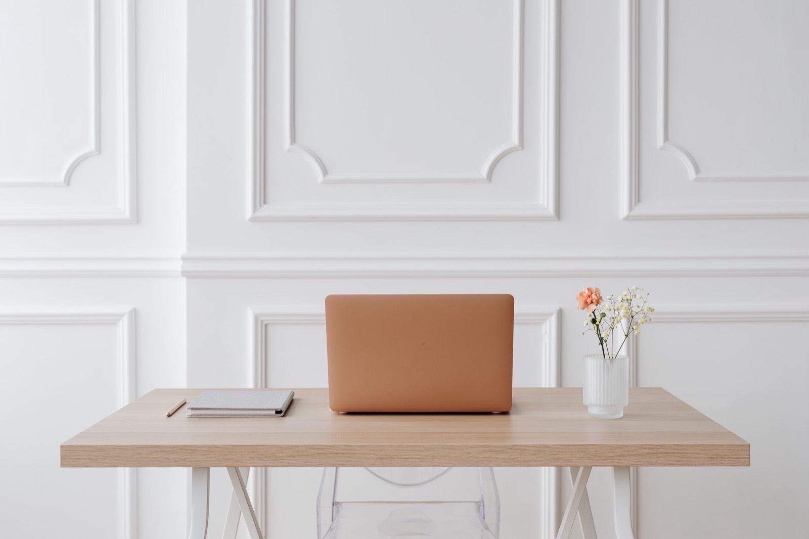 An empty office with one desk, a closed laptop and an empty chair in daylight.
